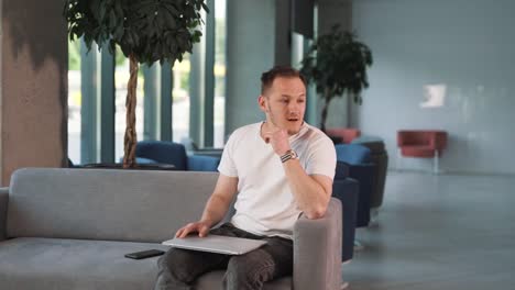 young man in the business center lobby, sitting with a laptop, wearily concludes his work, grasping his head with a depressed expression