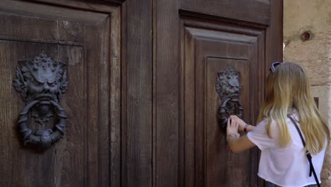 young blonde girl approaches old wooden door and tries to open it