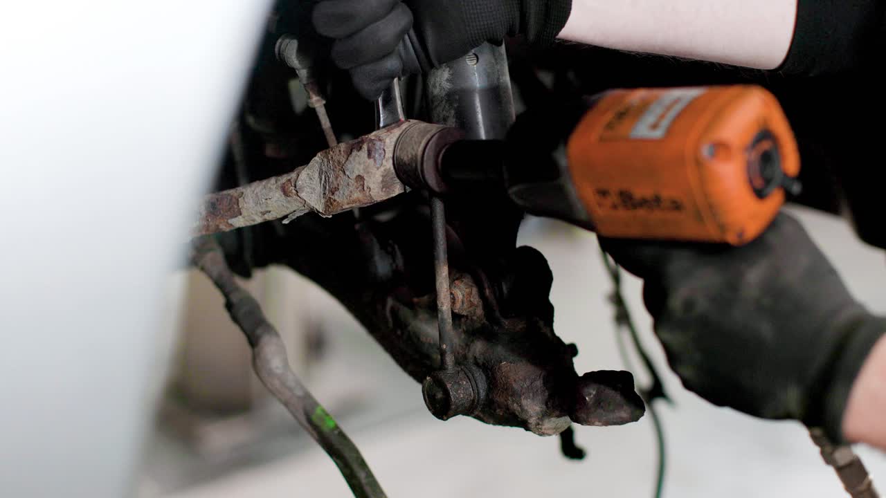 Meccanico che usa un utensile elettrico e una chiave inglese per rimuovere un tirante della barra stabilizzatrice dalla sospensione di un'auto. Ripresa statica in 4k