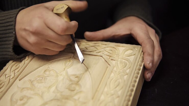 Hand-carved wood close-up. Unrecognizable craftsman carving wooden ornament on backgammon. Carpenter chiseling, shaping and sanding wood work for carved decoration