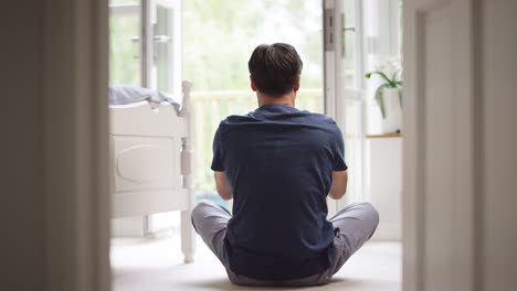 rear view of mature asian man in pyjamas sitting on bedroom floor meditating in yoga pose - shot in slow motion