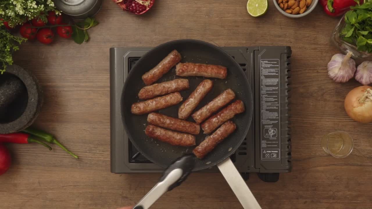 Crop person turning homemade sausages frying in pan