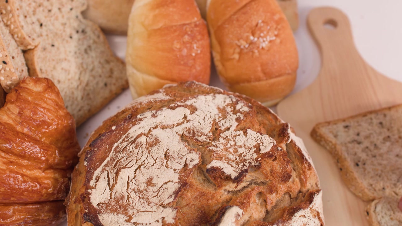 Hand picks up sliced multigrain bread from a wooden board near sourdough and croissants.