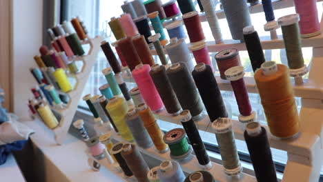 bobbins with colorful thread, measuring tape, pins in thimble, needle sticking out from heap of buttons, haberdashery, tools for sewing on pile