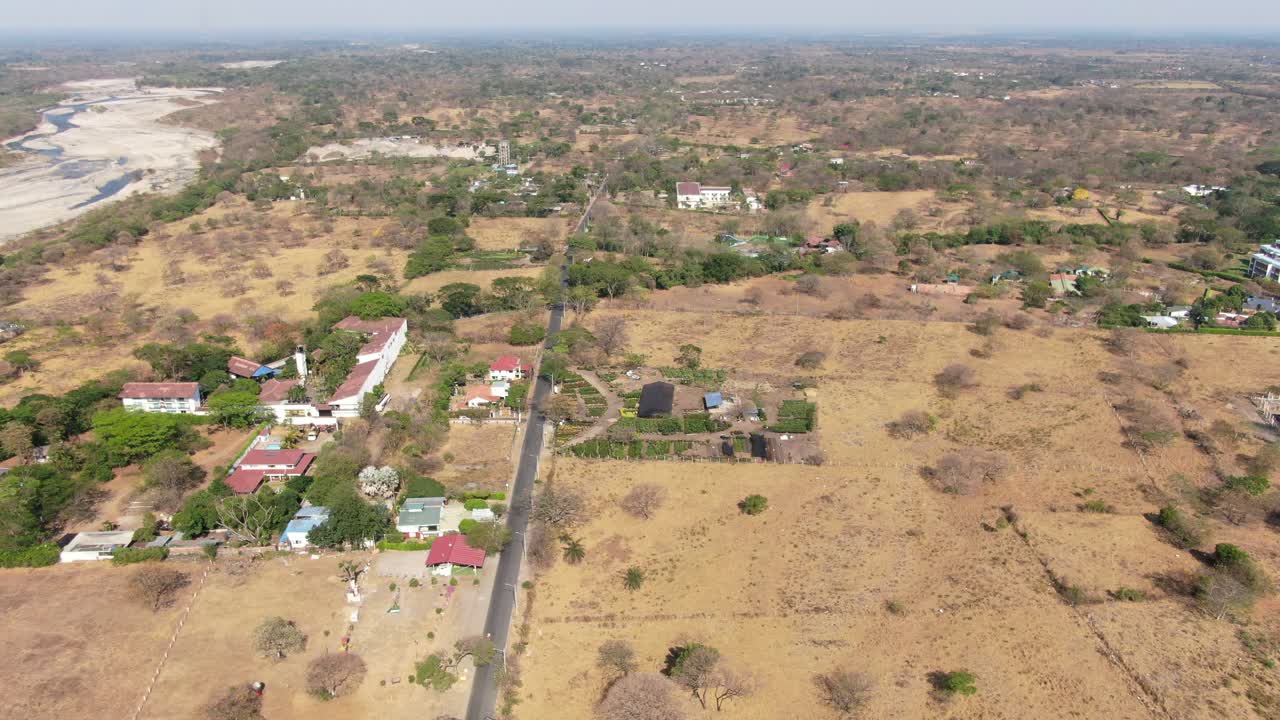 Linear black asphalt road with big houses in the dry environment of Yopal with in the background the dry river Rio Cravo Sur