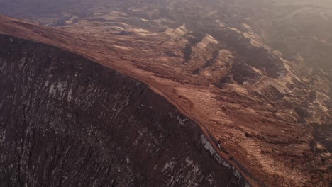 People-running-on-crater-rim-of-active-mount-bromo-vulcano-at-sunrise-golden-light,-aerial