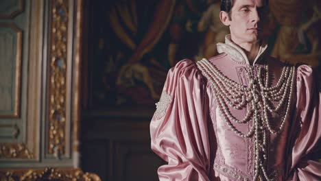 elegante noble con un lujoso traje de satén rosa y collares de perlas en capas de pie en medio de una habitación vintage adornada, rodeado de muebles antiguos y pinturas murales elaboradas