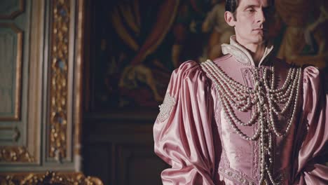 elegant nobleman wearing lavish pink satin suit and layered pearl necklaces standing amid ornate vintage room, surrounded by antique furniture and elaborate wall paintings