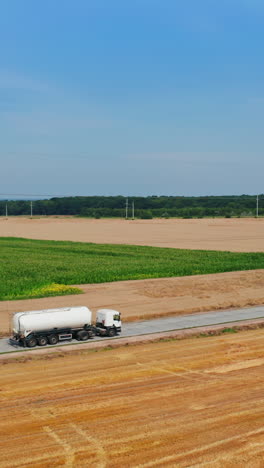 road crossing the agricultural farmlands and trucks going by it. tractor loaded with hay bales rides by the cut field. top view. vertical video