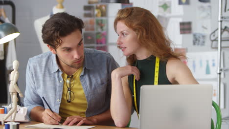 male and female clothes designers working on designs using laptop in fashion studio