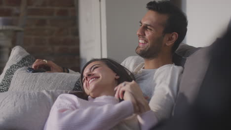 couple lying and relaxing on lounge sofa at home and watching tv together