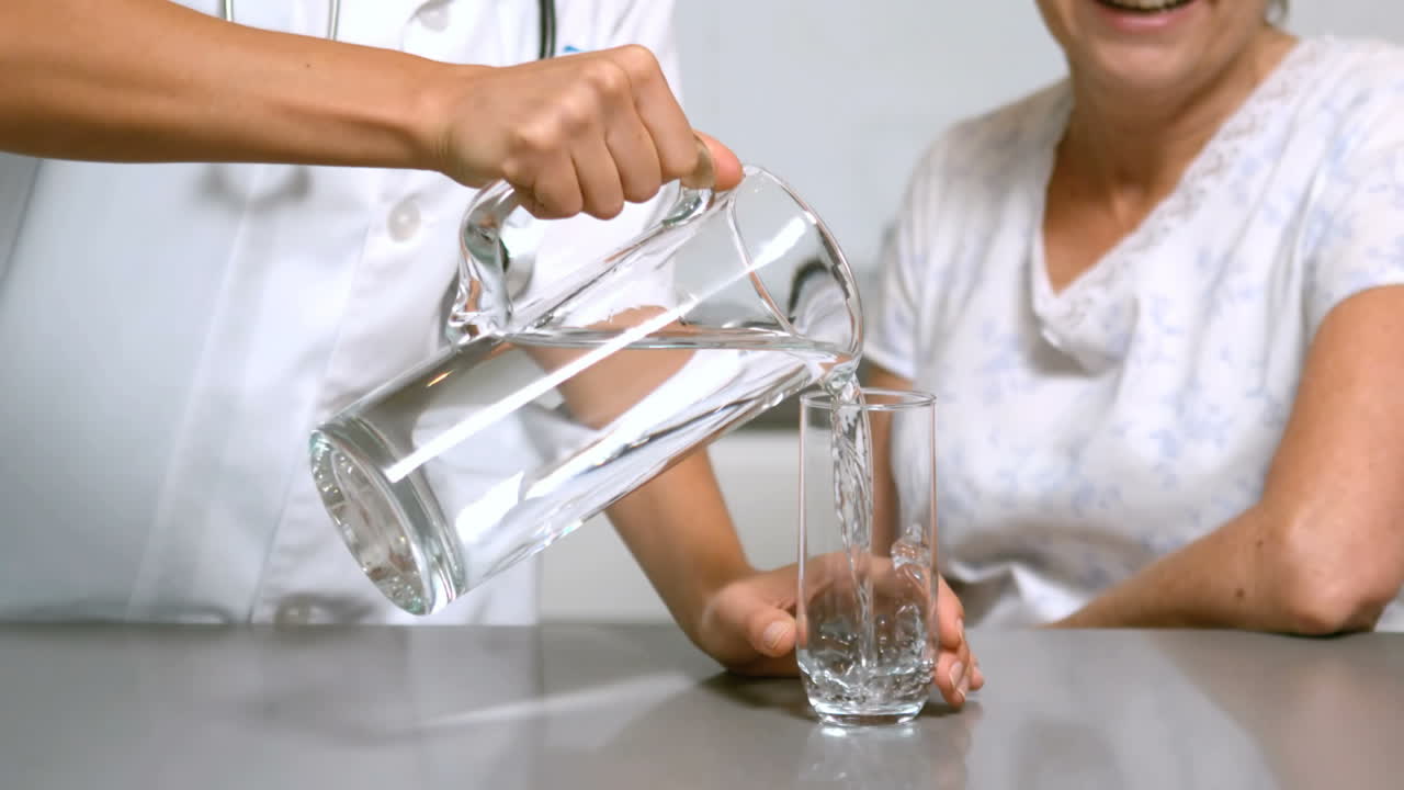 Premium stock video - Home help pouring water for patient in kitchen