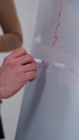 young businessman writing on a whiteboard. man and beautiful woman making new business plan and write the results on a board with a marker. vertical video