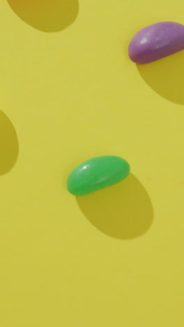 video of overhead view of rows of multi coloured sweets over yellow background