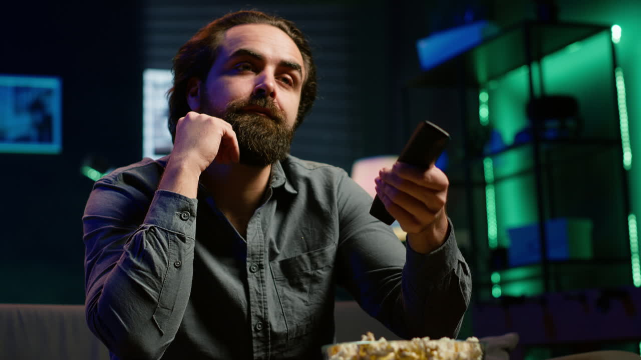 hombre aburrido comiendo palomitas de maíz y zapping a través de canales de televisión en la sala de estar iluminada rgb