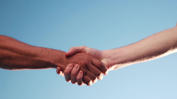 Due persone che si stringono la mano contro un cielo azzurro terso
