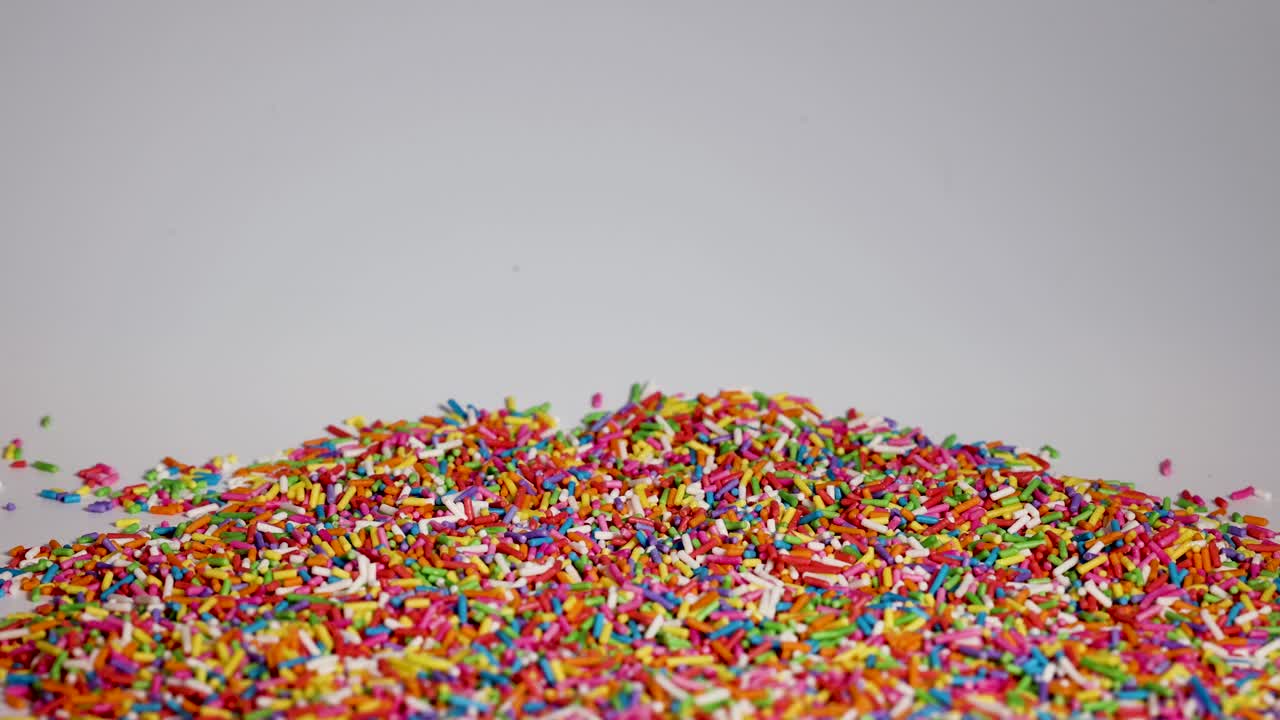Vibrant sprinkles cascade onto a pile, creating a colorful, dynamic scene against a neutral background