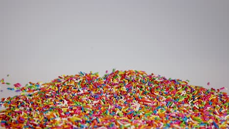 vibrant sprinkles cascade onto a pile, creating a colorful, dynamic scene against a neutral background