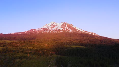 mount shasta is bathed in red, pink and yellow light at sunset