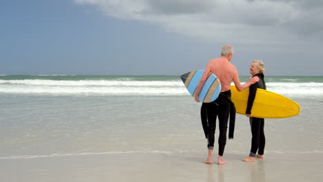 old caucasian senior couple holding surfboard at beach 4k