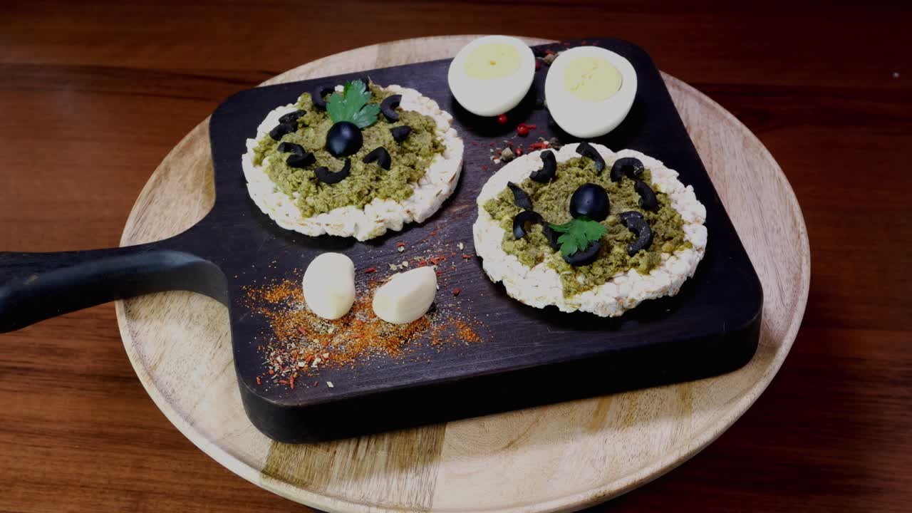 las tostadas de pastel de arroz con salsa de pesto verde y huevos hervidos giran lentamente en la tabla de cortar.