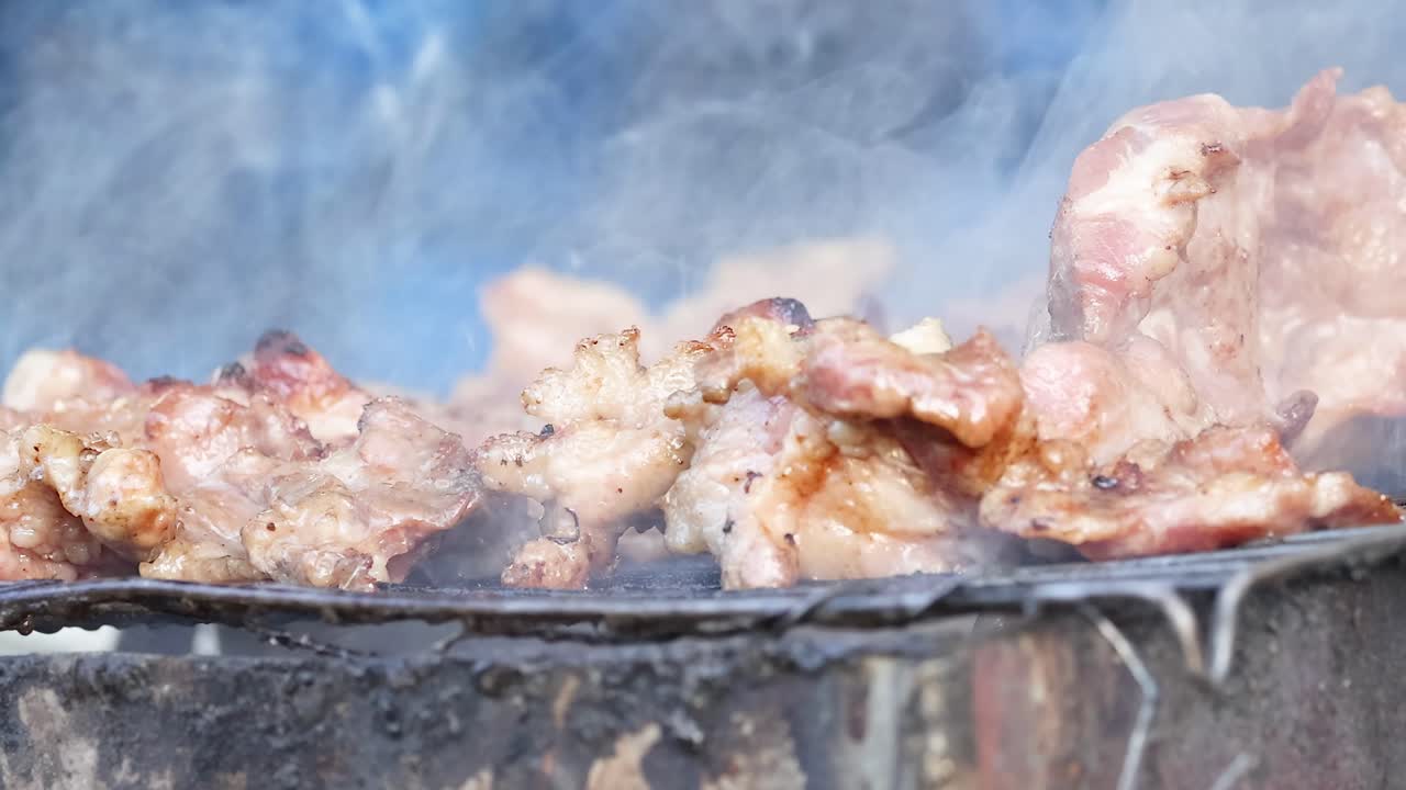 Close-up of pork pieces sizzling and smoking on a hot grill, capturing the essence of outdoor cooking.