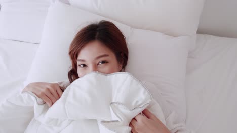 beautiful asian woman smiling under a blanket on a white mattress on the morning of the holiday