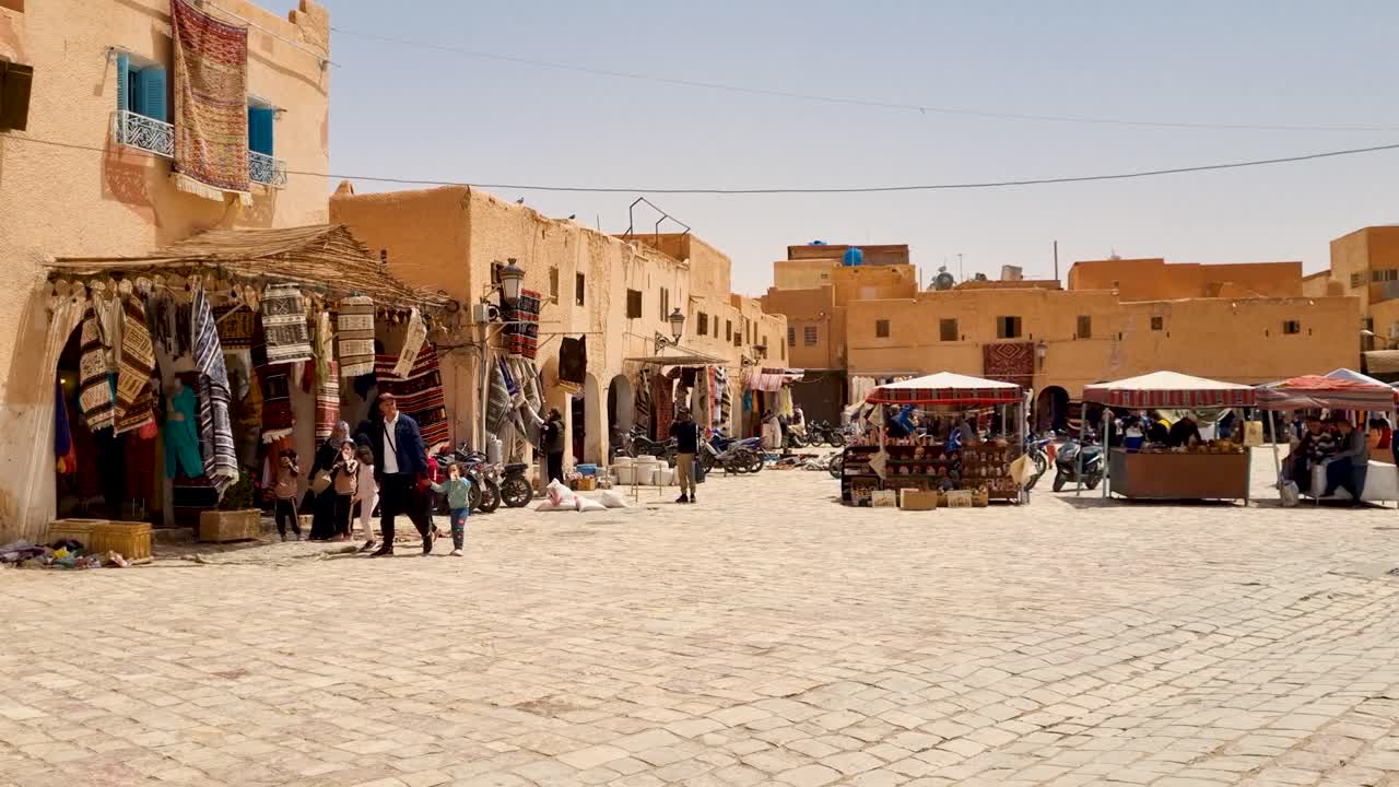 Shot of people, carpet shop and and traditional clay houses in the center of Saharan oasis town on a hot and sunny spring day in Ghardaia Algeria