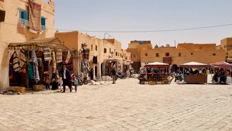 shot of people, carpet shop and and traditional clay houses in the center of saharan oasis town on a hot and sunny spring day in ghardaia algeria