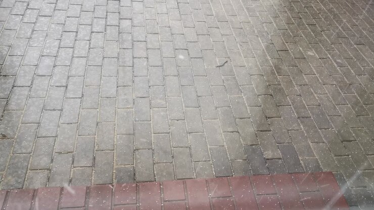 A small hail falls on the sidewalk near the house. The weather is bad outside.
