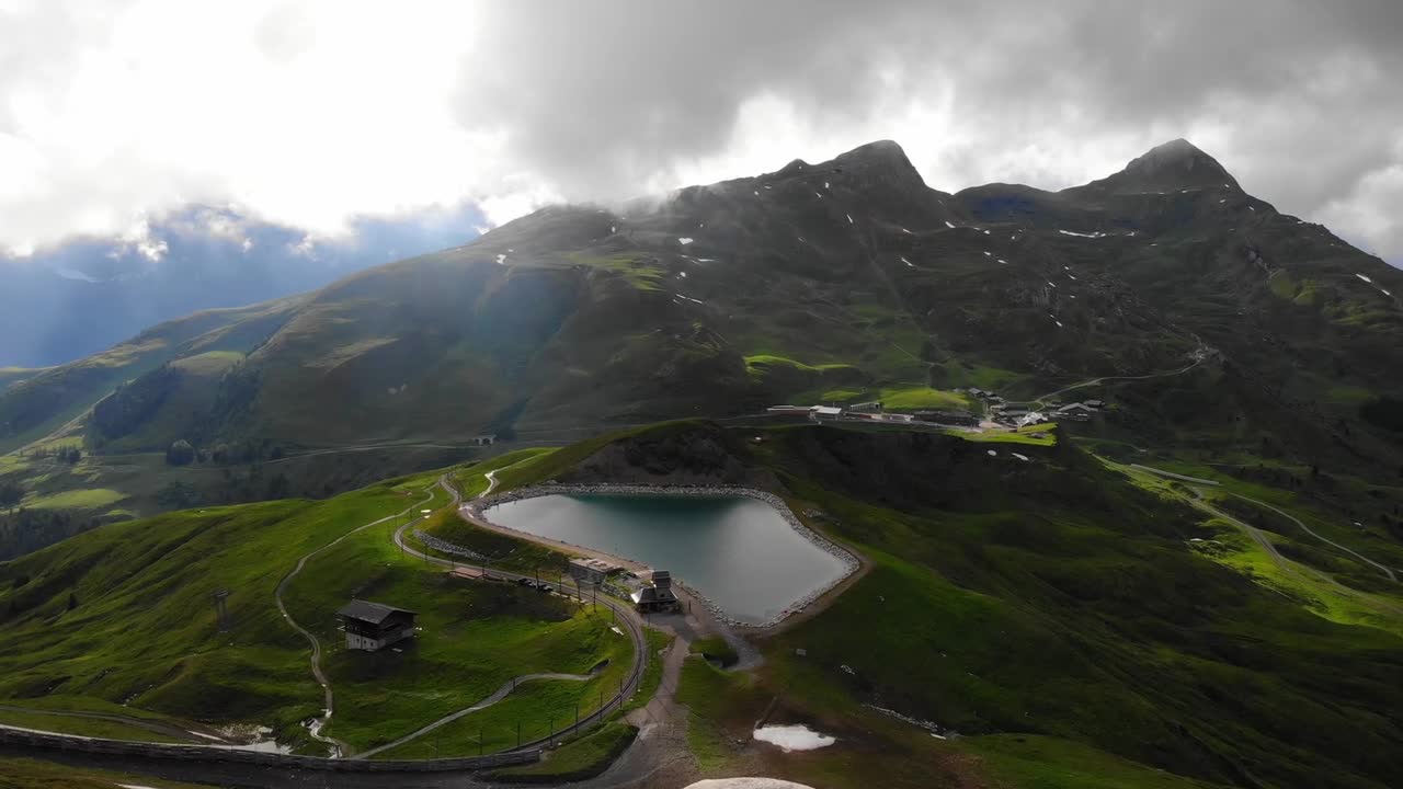 Drone view reveals small, serene lake nestled amidst majestic mountainous landscape in Iceland. The towering peaks encircle lake, while rugged terrain and lush greenery