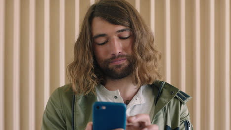 portrait-of-relaxed-friendly-young-caucasian-man-with-long-hair-texting-browsing-online-using-smarphone-social-media