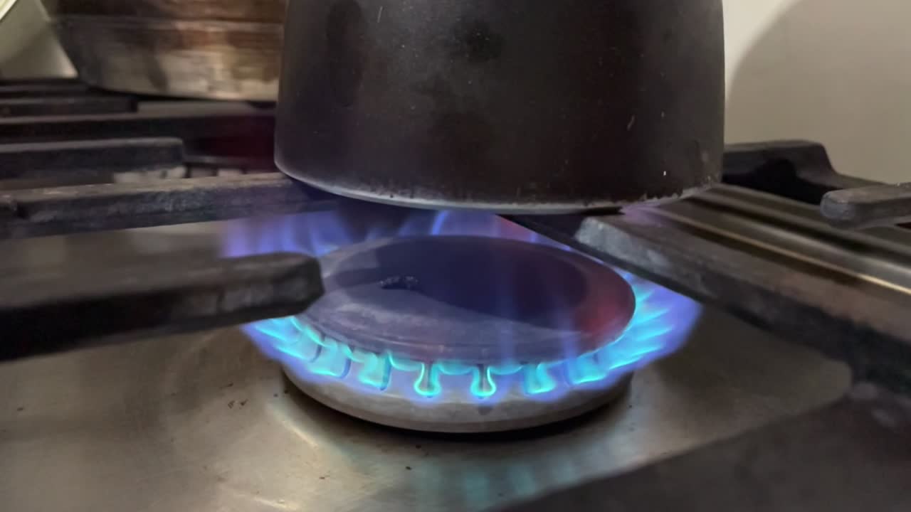Close up of gas burner igniting with blue flame in slow motion, italian moka pot placed on top