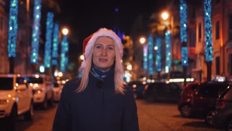 a beautiful woman in a santa claus hat walks at night on christmas