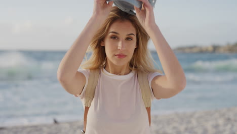 portrait of beautiful blonde woman on beach enjoying summer vacation looking at camera fixing hair wearing hat