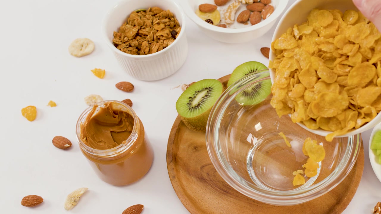 Close-up shot of crispy cereal pouring into a bowl surrounded by fresh fruit and nuts.