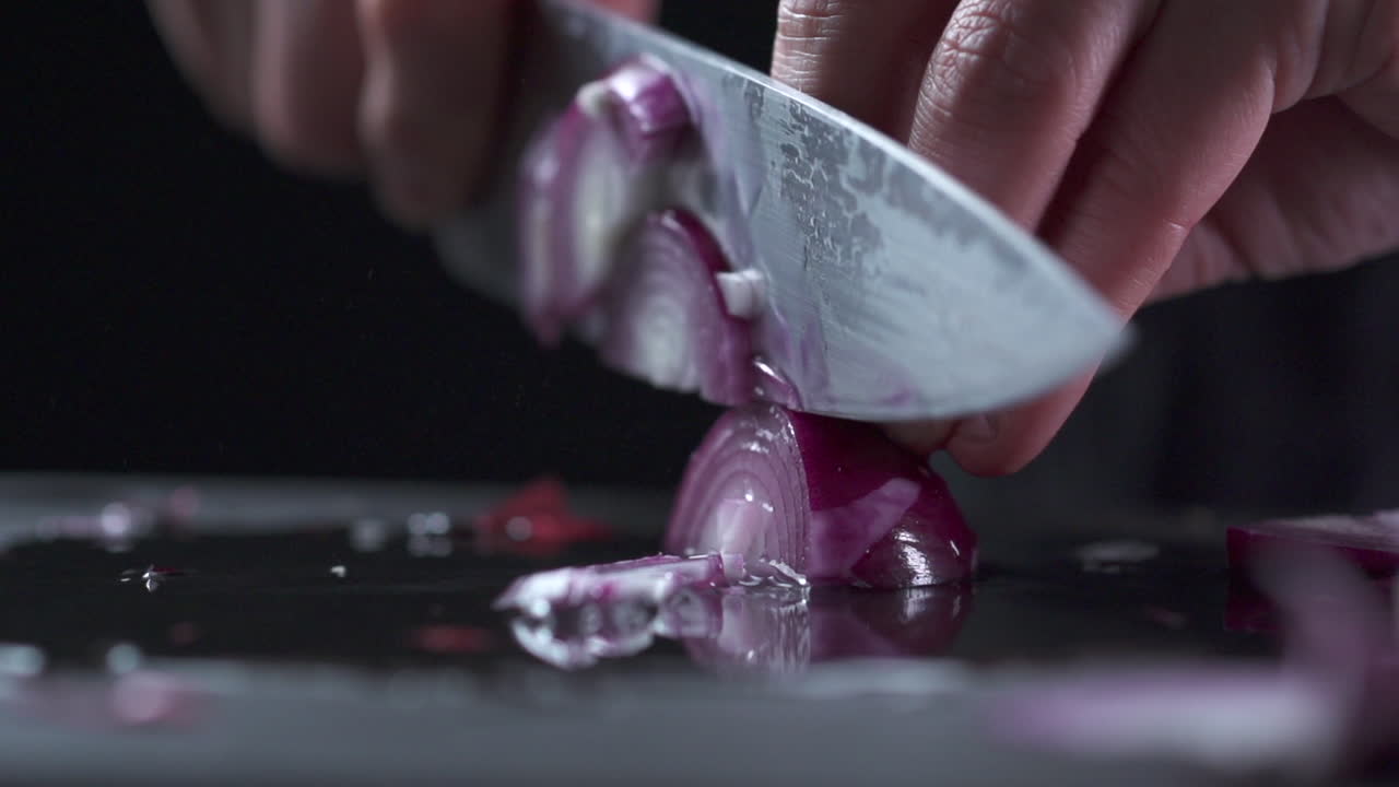knife cutting red onion on black backdrop in slow motion