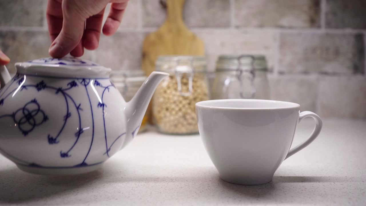 sirviendo una taza de té con las dos manos con ingredientes alimentarios en el fondo