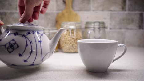 sirviendo una taza de té con las dos manos con ingredientes alimentarios en el fondo