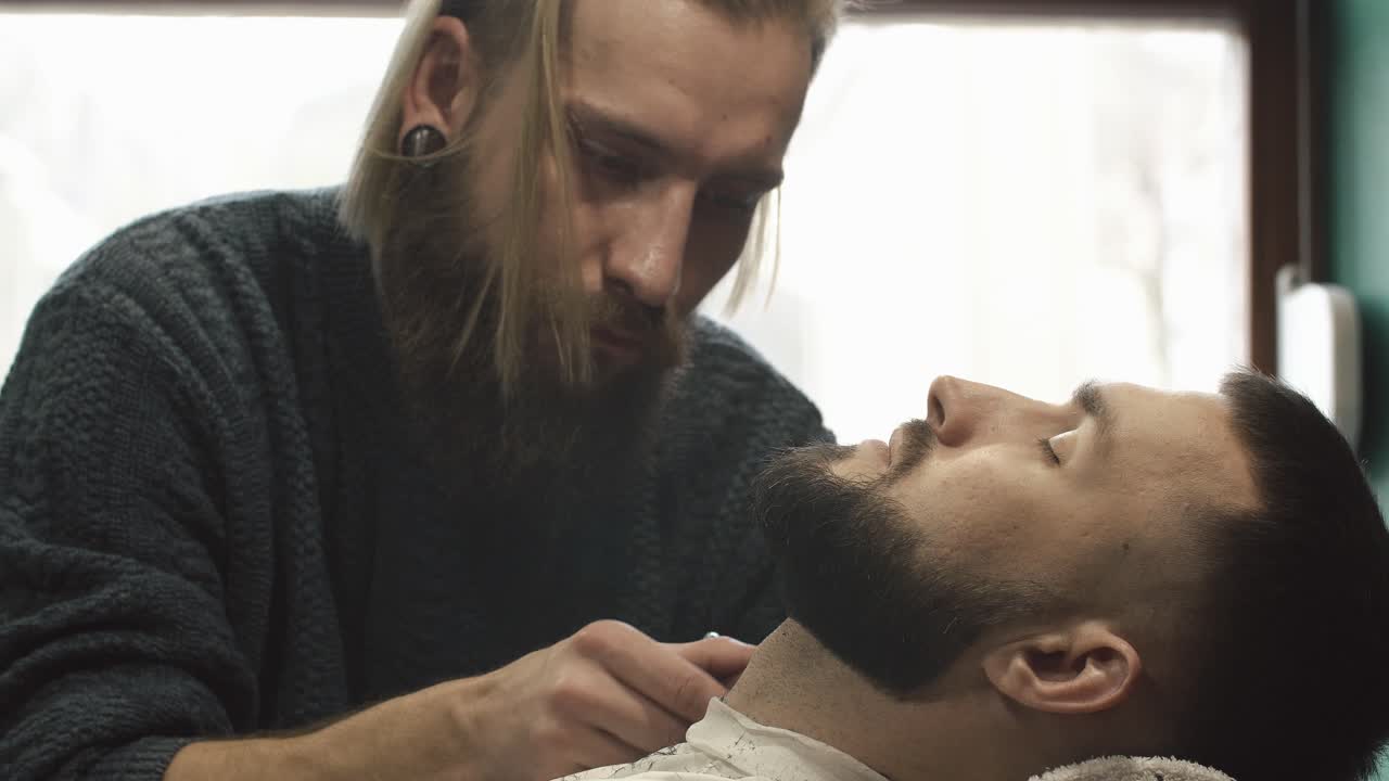 A barber trims and grooms a client's beard in a barbershop