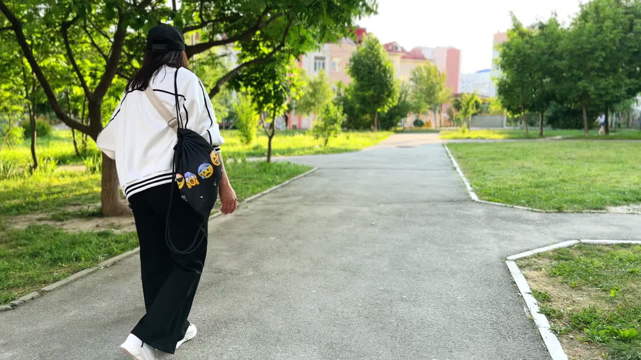 Mother follows her baby boy running by the park. Kid stops and takes mom's hand and they walk together.