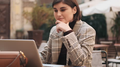 mujer de negocios trabajando en una computadora portátil en un café al aire libre.