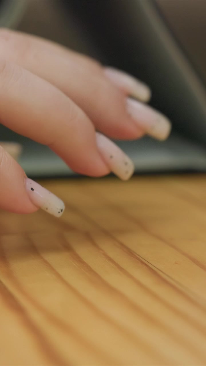 Close up of woman hand with light pink nails. Scene focuses solely on subtle motion of fingers over wood grain. Lighting is soft creating minimal shadows to highlight fine textures