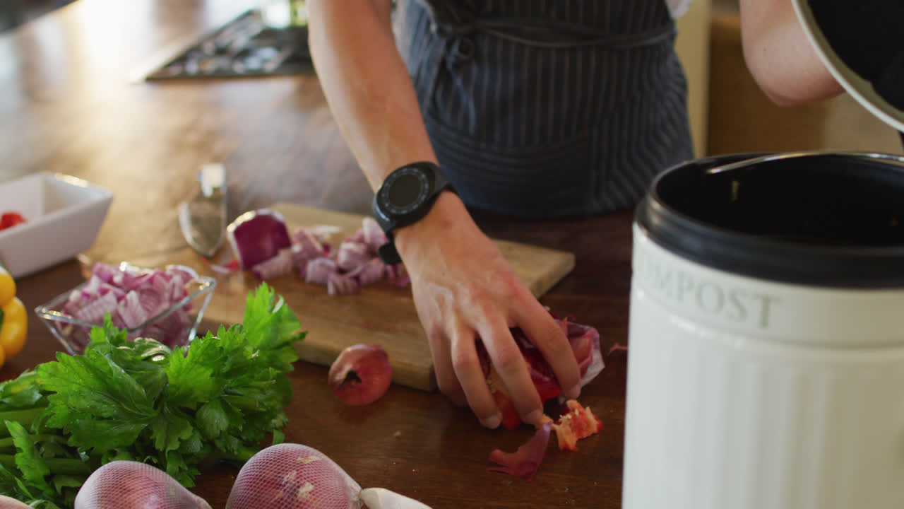 manos de una mujer caucásica embarazada con delantal, poniendo cáscaras en el contenedor de basura