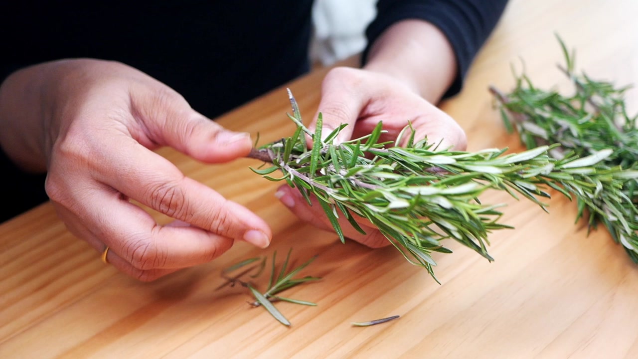 Hands Stripping Fresh Rosemary Leaves for Cooking on Wooden Table