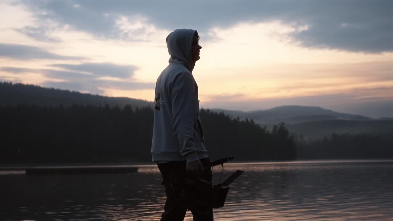 Man walking with a camera by the lake in Norway during a cloudy sunset