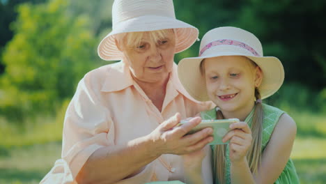 abuela y nieta usan el teléfono inteligente juntas para descansar en el parque en un día de verano 4k