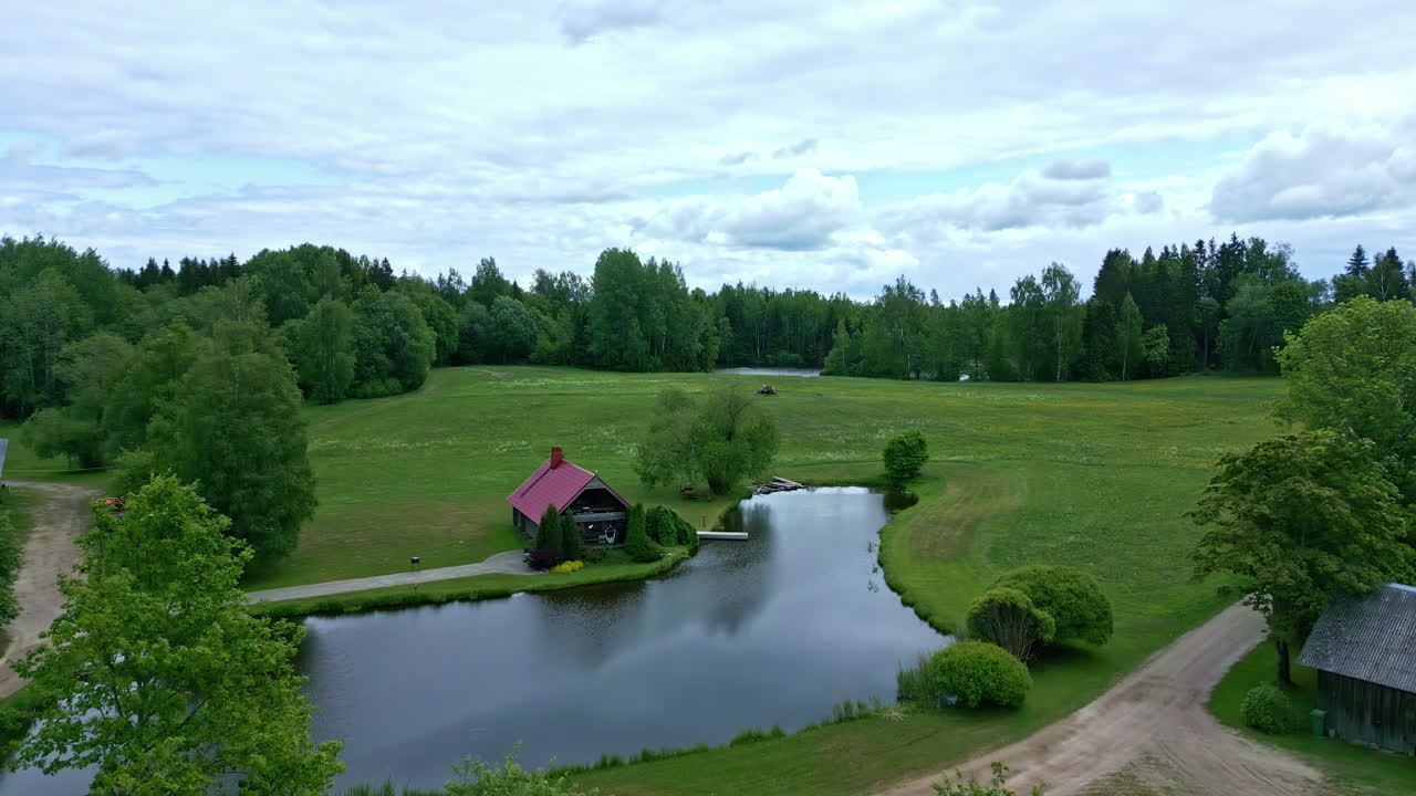 Droonin ilmakuva liikkuu eteenpäin kylämökkien yllä lammen rannalla maaseudulla illan aikaan.