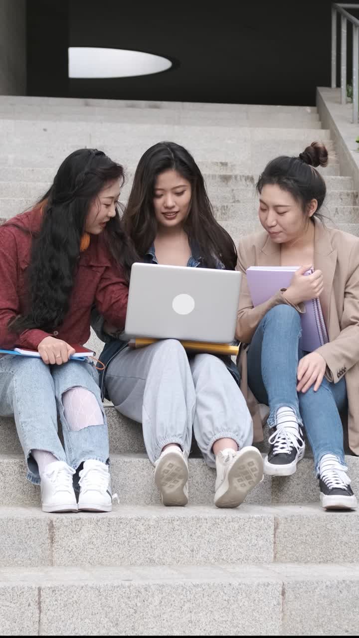 Gruppo di studentesse asiatiche che usano un laptop e studiano insieme sedute sulle scale del campus universitario