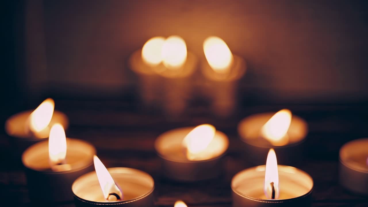 A serene video scene of lit candles, captured from a low angle. The soft glow creates a warm